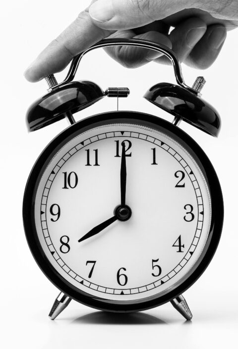 A classic black and white alarm clock being held by a hand, depicting the concept of time.