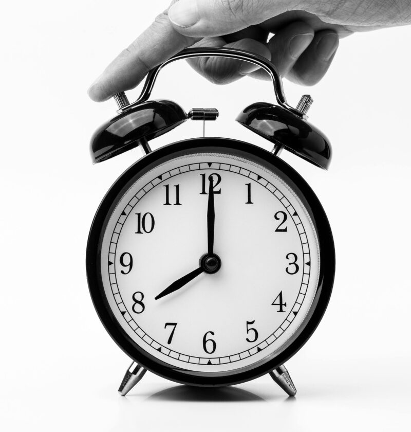 A classic black and white alarm clock being held by a hand, depicting the concept of time.