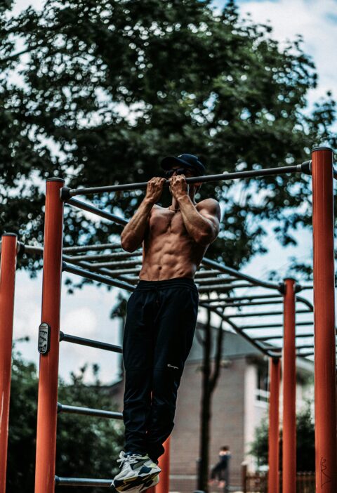 Athletic man performing pull-ups on a bar outdoors, showcasing fitness and strength.