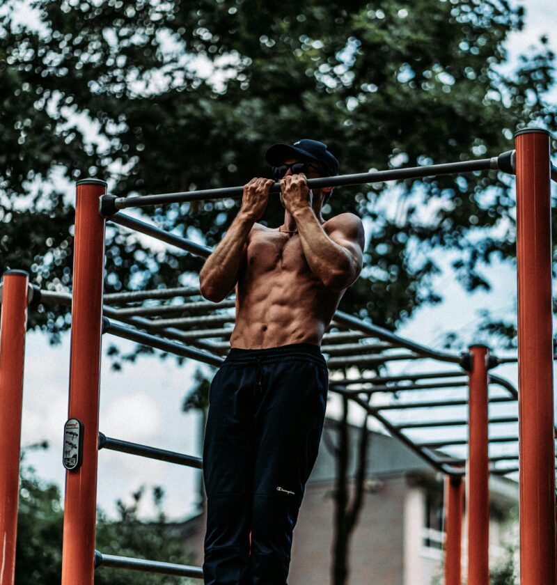 Athletic man performing pull-ups on a bar outdoors, showcasing fitness and strength.
