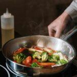 Close-up of sautéing broccoli and bell peppers in a pan on a stove.