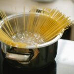 Raw spaghetti cooked in boiling water in saucepan placed on stove in light kitchen