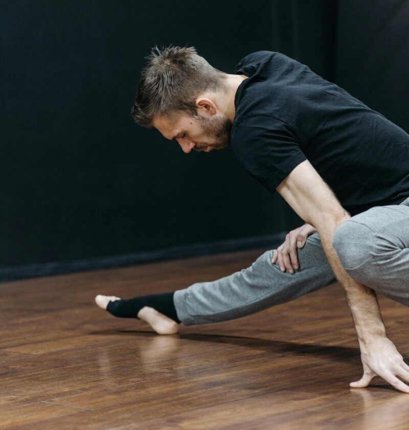 Mid-adult man stretching in a dance studio, emphasizing flexibility and balance.
